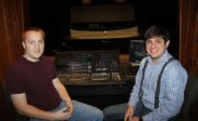 Two men seated beside a theater lighting and sound control console