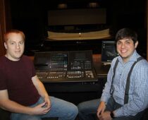 Two men seated beside a theater lighting and sound control console