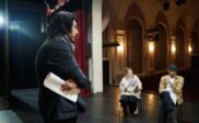 Director holds a script while guiding actors during a theater rehearsal