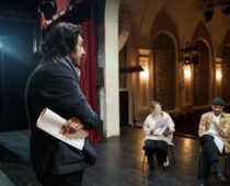Director holds a script while guiding actors during a theater rehearsal