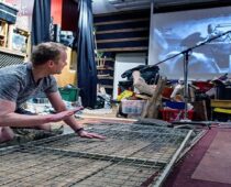 Man arranging a metal grid amid theatrical props and recording equipment