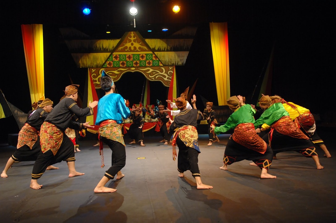 Traditional Indonesian puppet theater (wayang kulit) performance with dancers in traditional costumes performing in front of an ornate puppet theater stage with colorful lighting and decorative backdrop.