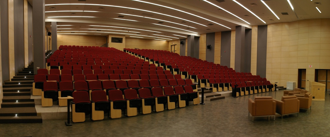 Interior view of a modern theater auditorium showing tiered red seating arrangement, professional lighting, and clean architectural design typical of managed performing arts venues.